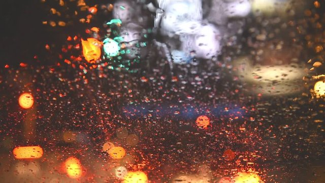 Rains drop on front of car glass window with Street Bokeh Lights of traffic light. Out Of Focus Background.