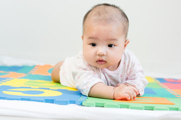 Portrait of adorable baby with saliva lying on the tummy on colorful eva foam, indoors