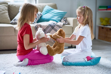 Side view portrait of two little girls playing with plush teddy bears sitting on floor  at home in...