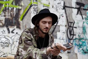 Attractive trendy-looking young European man with beard and long hair wearing hat and stylish...