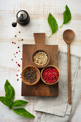 Red, white and black peppers, basil leaves, simple old spoons and linen napkin  on  old wooden stand. Kitchen accessory concept. Selective focus. Top view. Toned image.