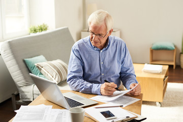 Portrait of modern senior man filling in application form  at home sitting at table with laptop in ...