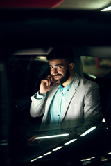 Handsome elegant businessman is looking through the window of the car while talking on a mobile.