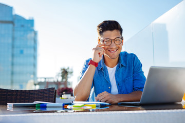 Charming college guy smiling into camera while working on hometask