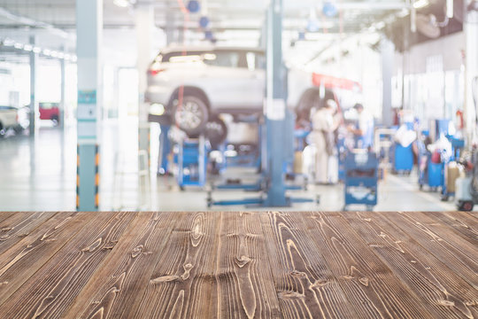 Brown wooden table free space and blurred background of car technician repairing the car in the shop, garage or service station. Use for product display or product montage design