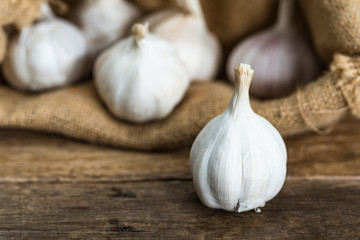 white garlic with blurred garlics in gunny sack cloth background on brown wooden table, selective focus