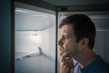 Hungry man is looking for food in empty fridge at night.