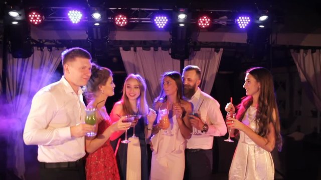 Young friendly people toasting with cocktails in the open air night club