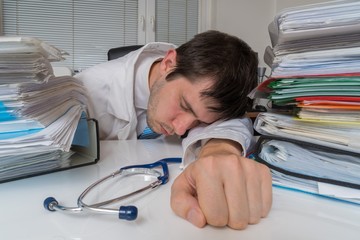 Tired and overworked doctor is sleeping on desk in office.