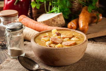 Wooden bowl of split pea soup with sausage and potatoes