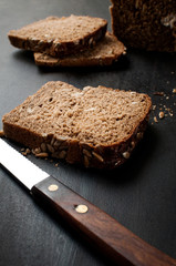 Fototapeta na wymiar fried slices of fresh bread with sunflower seeds and a knife on a dark table, horizontal image