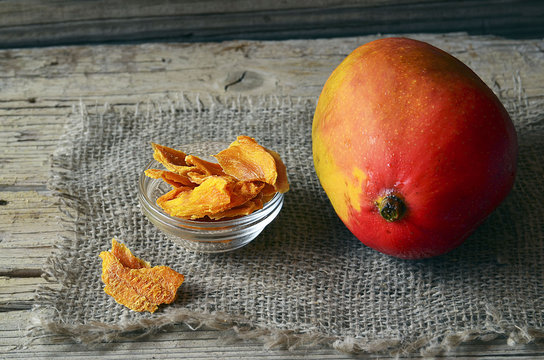 Raw organic dried mango in a glass bowl and fresh ripe mango fruit on wooden rustic table.Dried mangos.Selective focus.