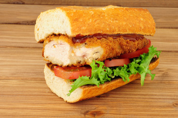 Southern fried chicken steak sandwich with fresh salad on a wood background