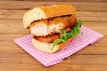 Southern fried chicken steak sandwich with fresh salad on a wood background