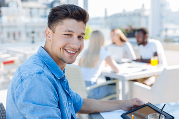 Positive minded guy with tablet computer working in cafe