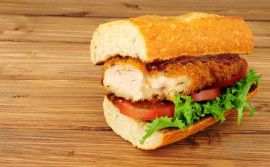 Southern fried chicken steak sandwich with fresh salad on a wood background