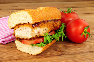 Southern fried chicken steak sandwich with fresh salad on a wood background