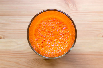 Fresh carrot juice with bubbles in a glass cup on a wooden table, top view, close-up