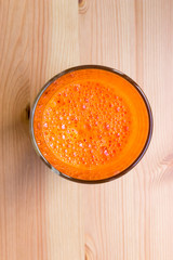 Fresh carrot juice with bubbles in a glass cup on a wooden table, top view, close-up