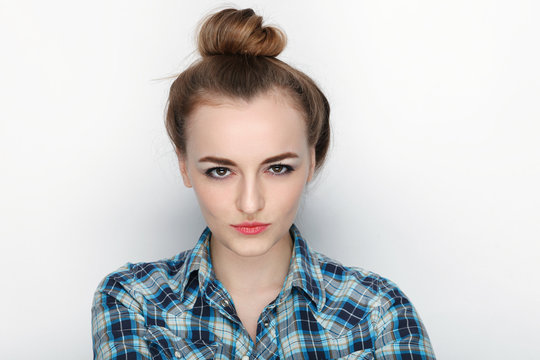 Beauty portrait of young adorable fresh looking blonde woman with high bun hair chaos in blue plaid shirt. Emotion and facial expression concept.