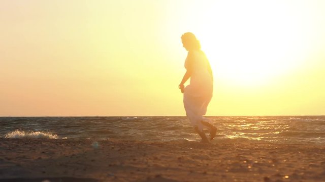 Beach woman running to water in dress at sunset raising arms enjoying freedom during summer holidays vacation travel. Beautiful happy Caucasian female girl outside. Slow motion.