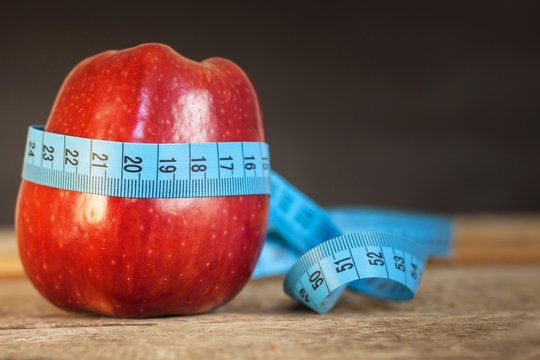 Red apple with measuring tape to measure length on a wooden background, diet, healthy lifestyle.