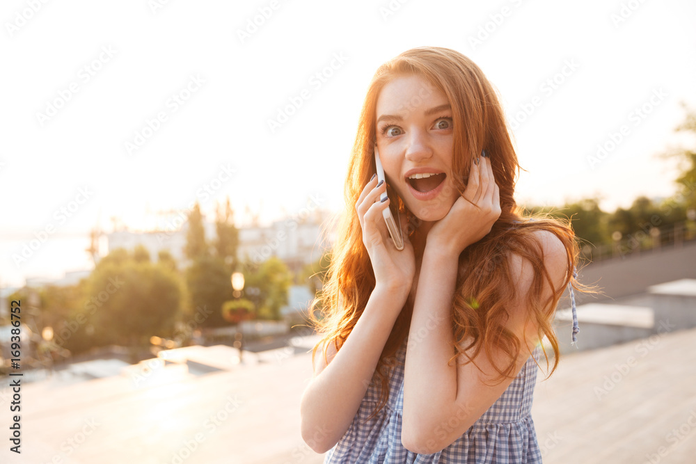 Sticker Amazed pretty redhead girl with long hair talking on phone