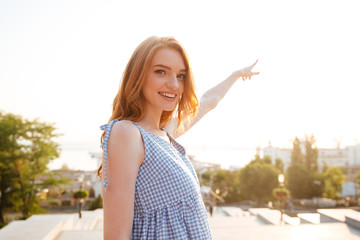 Smiling pretty girl pointing finger away while standing outdoors