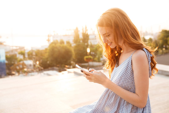 Pretty Smiling ginger woman in dress using smartphone