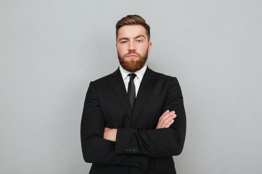 Confident young businessman in suit standing with arms folded