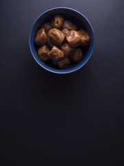 Umeboshi plums from Japan in blue bowl, fermented and salted and placed in a honey syrup. Isolated on black background