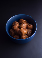 Umeboshi plums from Japan in blue bowl, fermented and salted and placed in a honey syrup. Isolated on black background