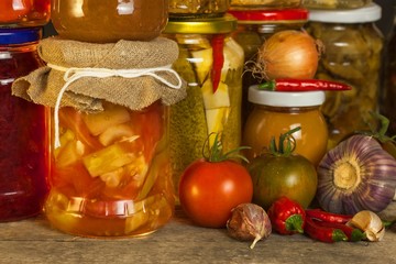 Jars with marinated food and organic raw vegetables. Preserved vegetables on wooden background. Various marinaded food. Life on a rural farm.
