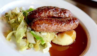Sausage and mashed potato with seasonal greens served with red wine gravy on a white plate