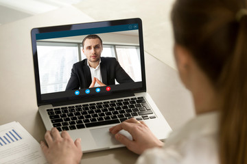 Fototapeta na wymiar Businesswoman calling businessman online by video chat computer app, partners negotiating online on virtual meeting, employee reporting to boss running business remotely, close up rear view