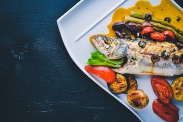 Fish trout baked with grilled vegetables. On a wooden background. Top view. Free space for text.