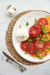 Fresh tomato salad with burrata cheese (mozzarella) and basil. White wooden rustic table
