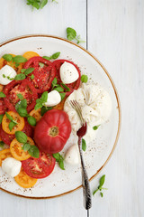 Fresh tomato salad with burrata cheese (mozzarella) and basil. White wooden rustic table
