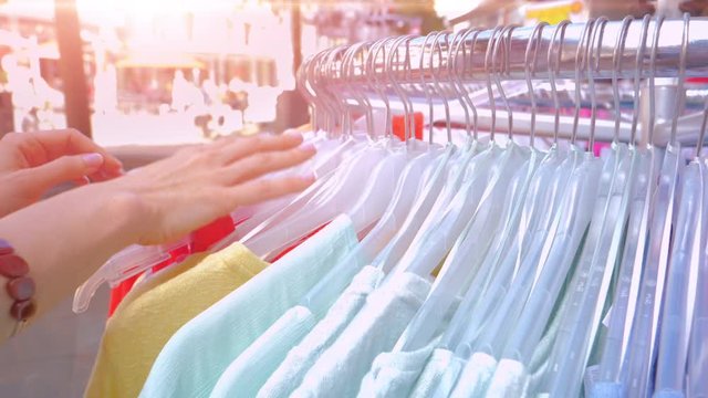 Woman in the shop looks through the female shirts, which are hanging on the racks