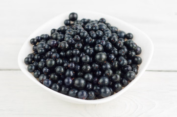 Many fresh ripe blackcurrant in white bowl on old white rustic wooden planks