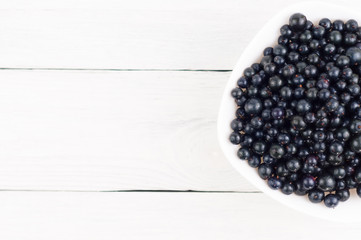 Many fresh ripe blackcurrant in white bowl on old white rustic wooden planks