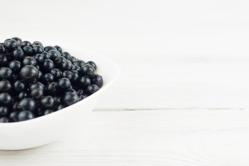 Many fresh ripe blackcurrant in white bowl on old white rustic wooden planks