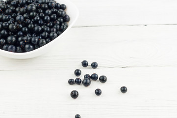 Many fresh ripe blackcurrant in white bowl and scattered on old white rustic wooden planks