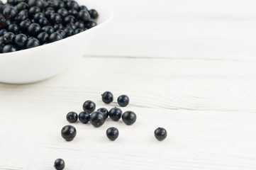 Many fresh ripe blackcurrant in white bowl and scattered on old white rustic wooden planks