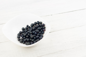 Many fresh ripe blackcurrant in white bowl on old white rustic wooden planks