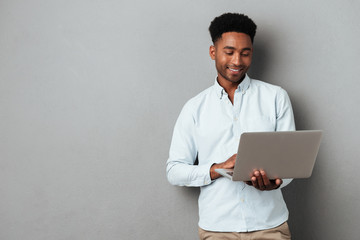 Young smiling african man standing and using laptop - Powered by Adobe