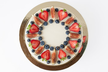 Cake with whipped white cream, decorated with fresh strawberries, blueberries and figs. Picture for a menu or a confectionery catalog. Isolated. Top view.