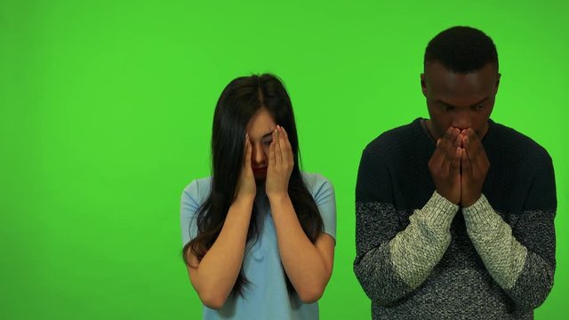 A young Asian woman and a young black man cover their faces with their hands, then stop and look around, confused - green screen studio