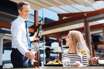 Cheerful professional waiter putting a glass on the table
