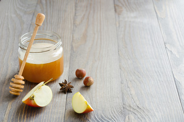 Jar of honey with honey stick, slices of apple, hazelnuts and anise